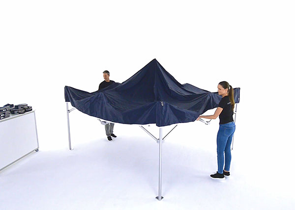 Two persons simply spread apart the folding tent to assemble it.