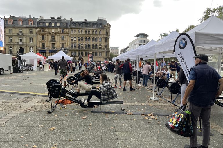 People rowing on rowing ergometers under Pro-Tent folding tents on the forecourt of the Frankfurt Opera House.