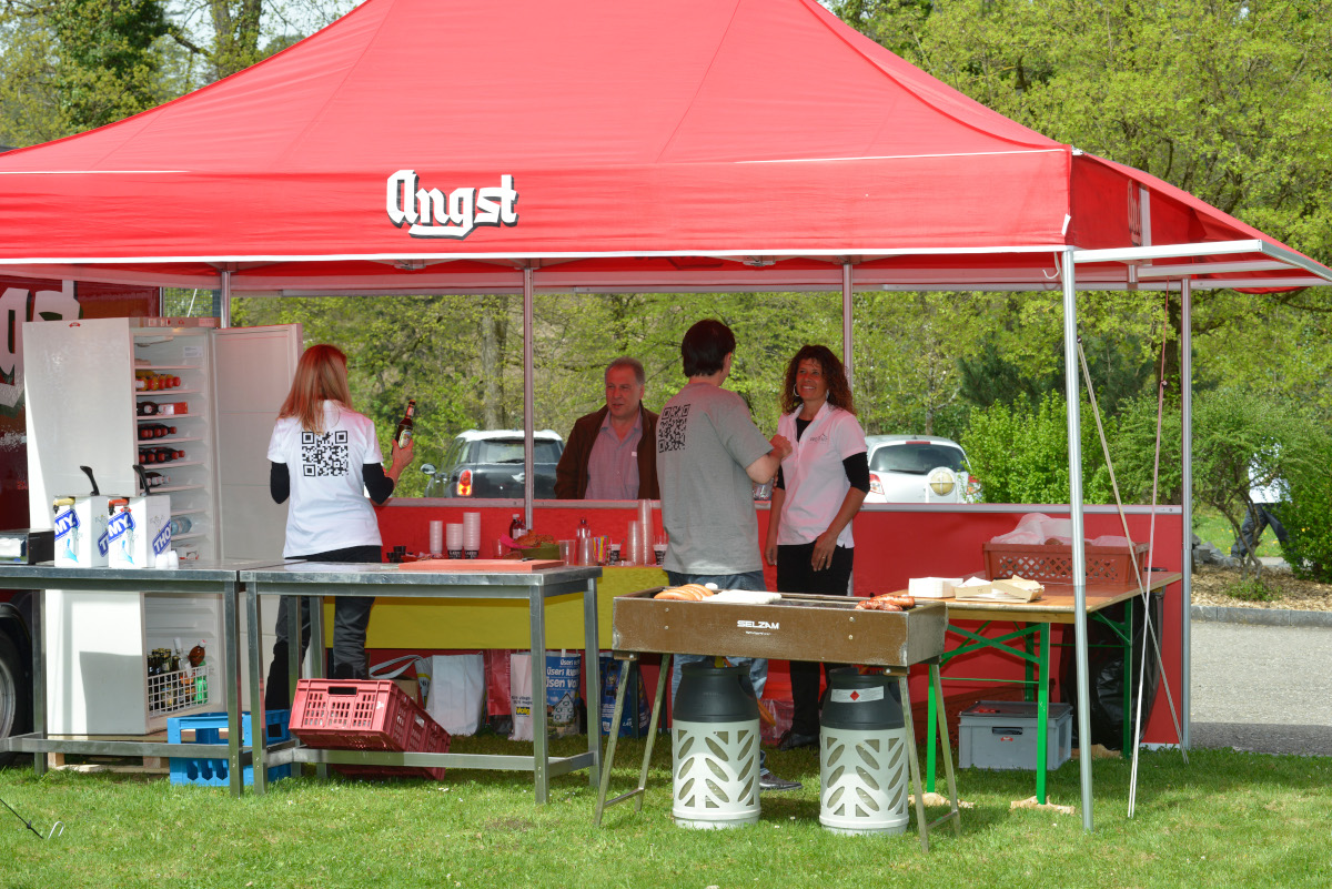 A catering stand, set up under a folding tent, offers fresh grilled food.