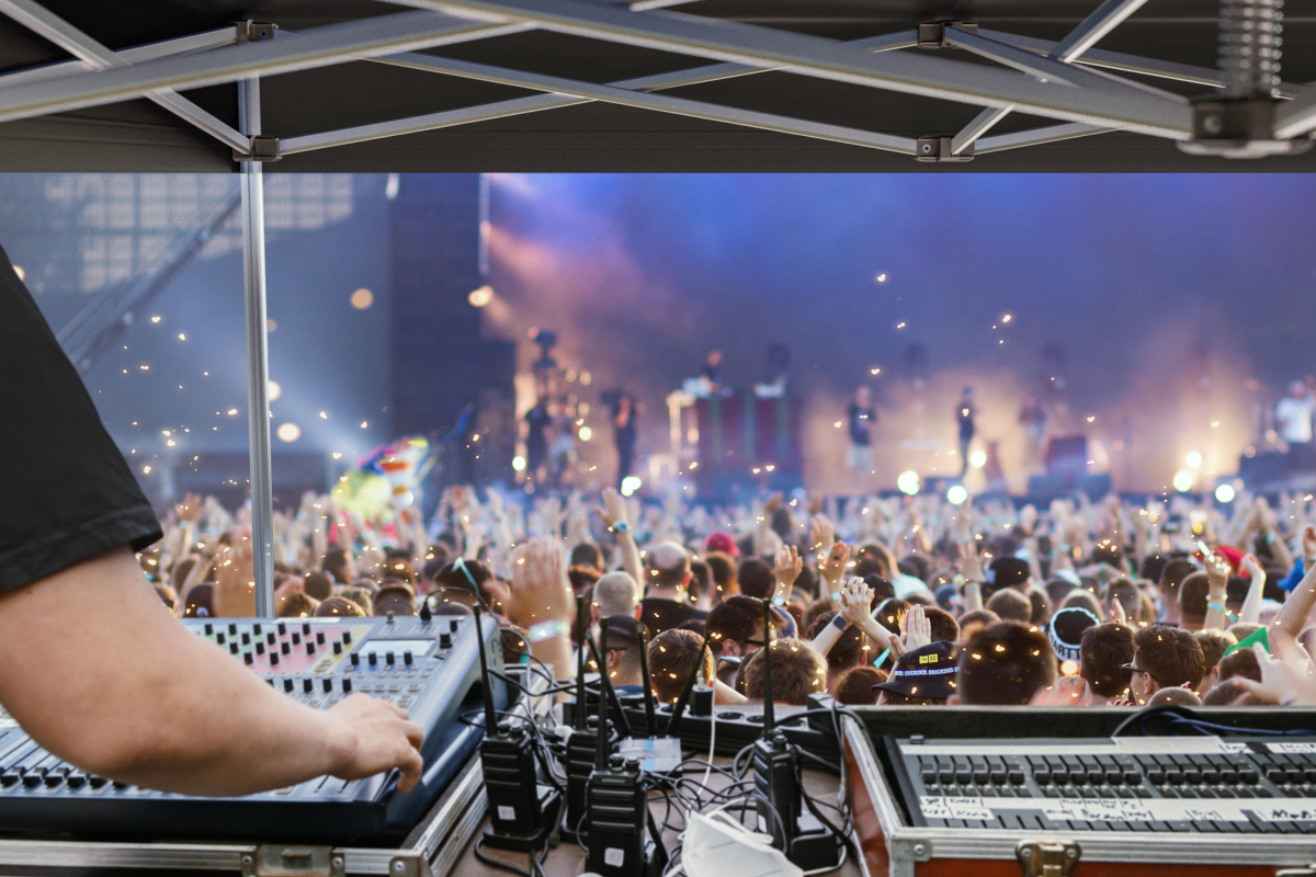 A technician operating the mixing console under an FOH tent at an open-air concert.