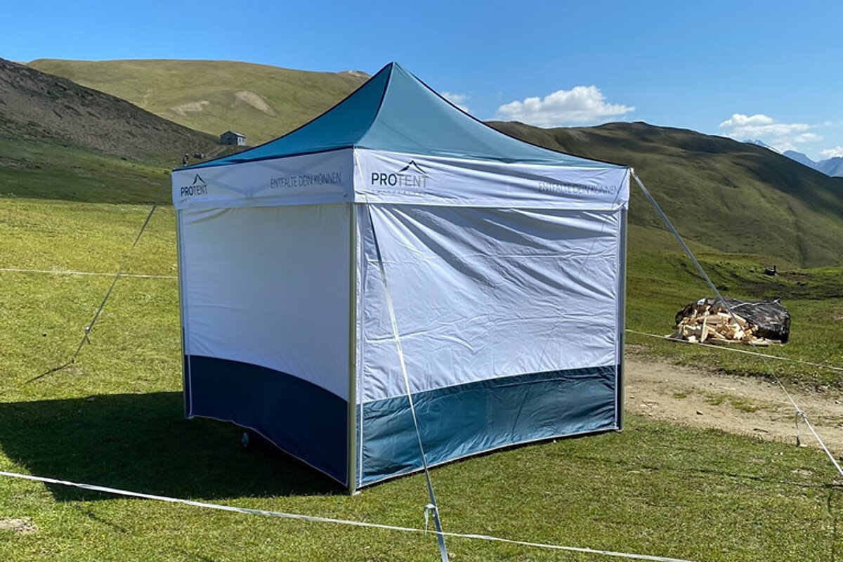 Ein Pro-Tent Faltzelt mit Seitenwänden als Sonnenschutz steht auf einer sonnigen Wiese.