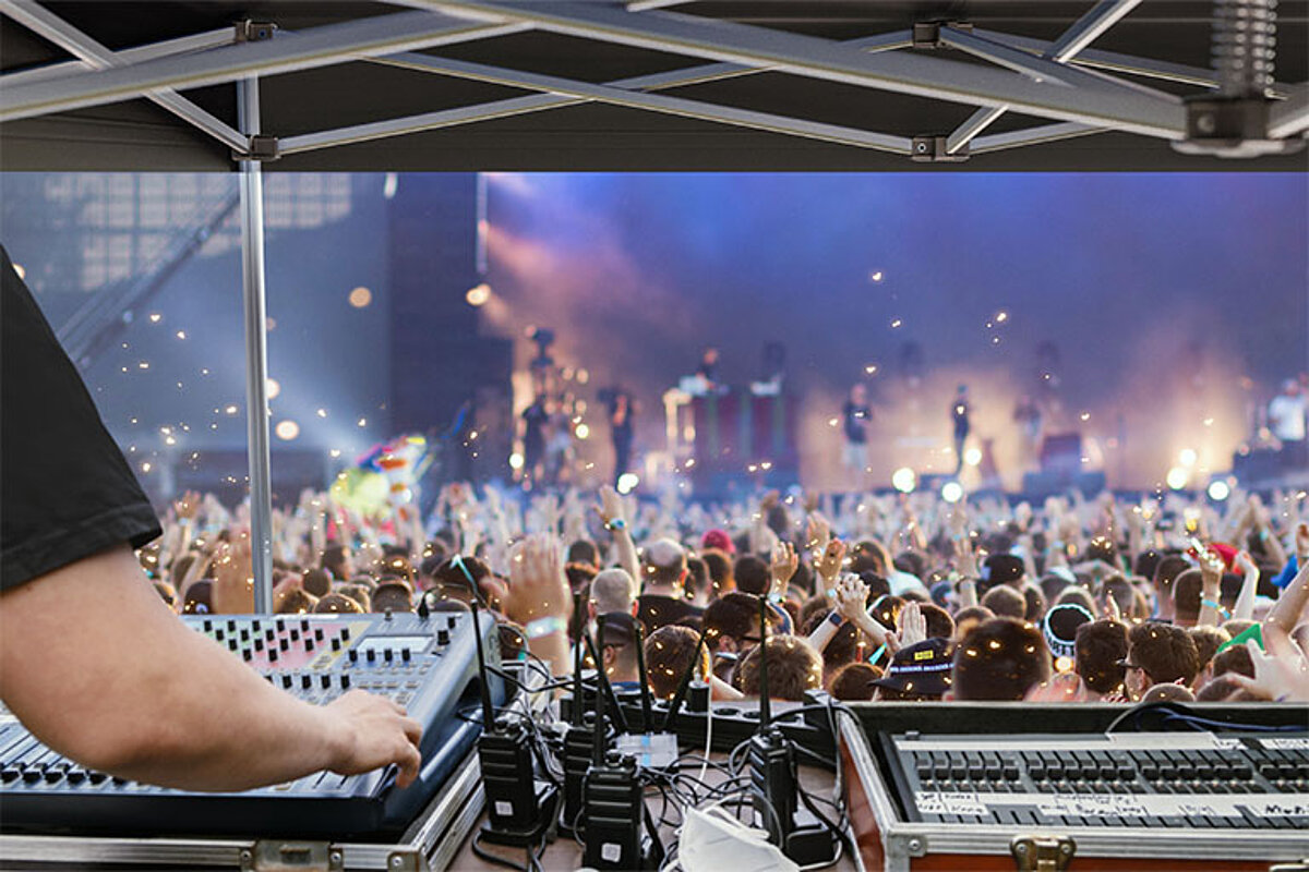 Ein Techniker bedient unter einem FOH-Zelt das Mischpult bei einem Open-Air-Konzert.