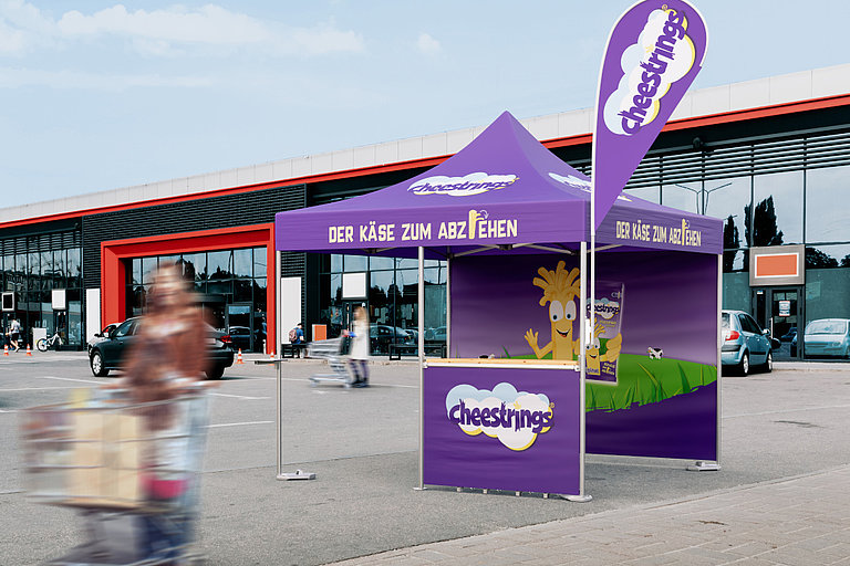 An advertising stand of the company cheestrings in front of a shopping centre.