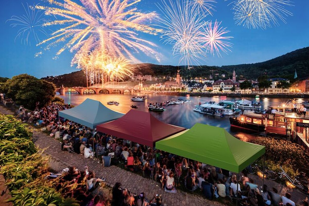 Trois tentes pliables sont utilisées comme abri pour des personnes debout lors d’une fête dans un port.