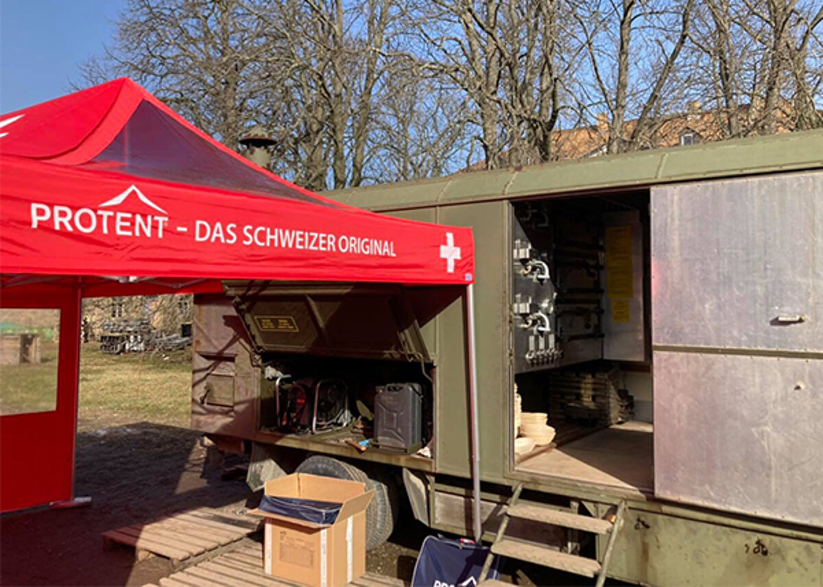 The Pro-Tent folding tent ideally complements the baking vehicle of the Herzensbäckerei. A red Pro-Tent folding tent in front of a former army baking vehicle that was refurbished by Herzensbäckerei.