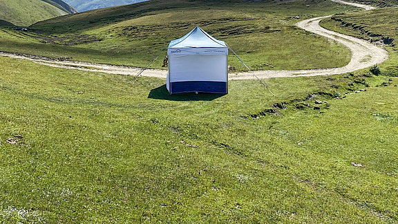A folding tent stands on a green field.