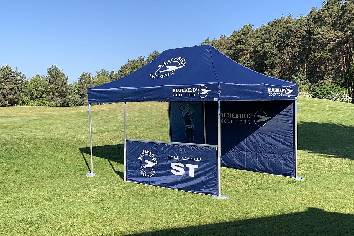 The folding tent was designed using the CI of the Bluebird Golf Tour. The blue Pro-Tent 5000 from FairwaySports on the grass.